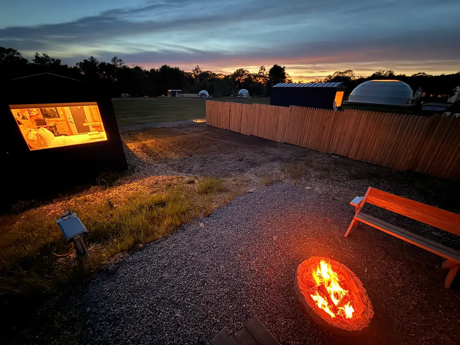 A lit Pine cabin and a firepit at dusk on a wooded campground