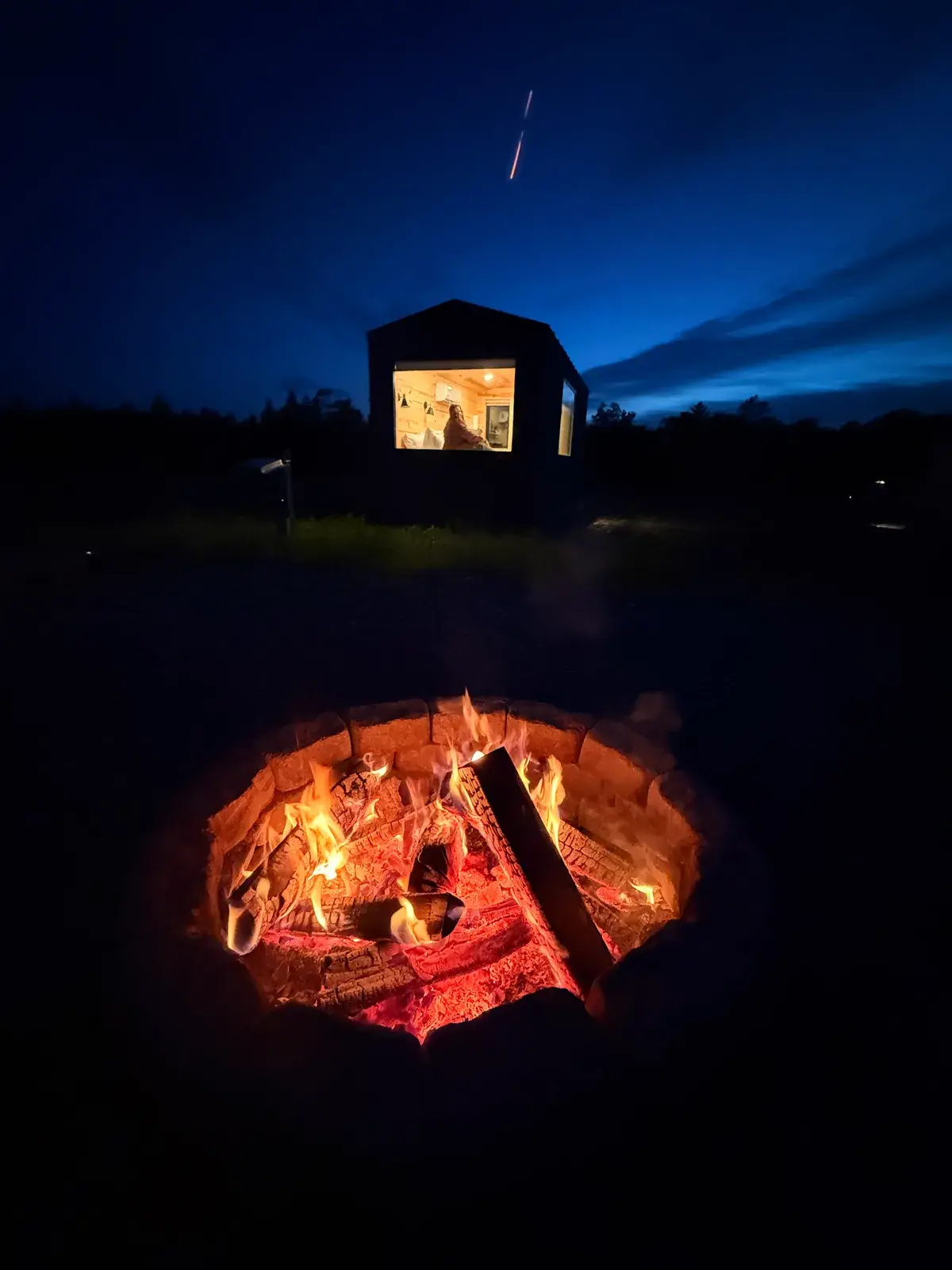 A Pine cabin glowing at night beside a firepit on a campground